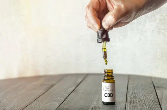 Hand holding pipette with CBD oil on wooden table