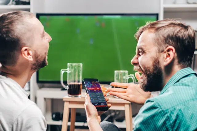 Two male friends watching live football game broadcast on tv