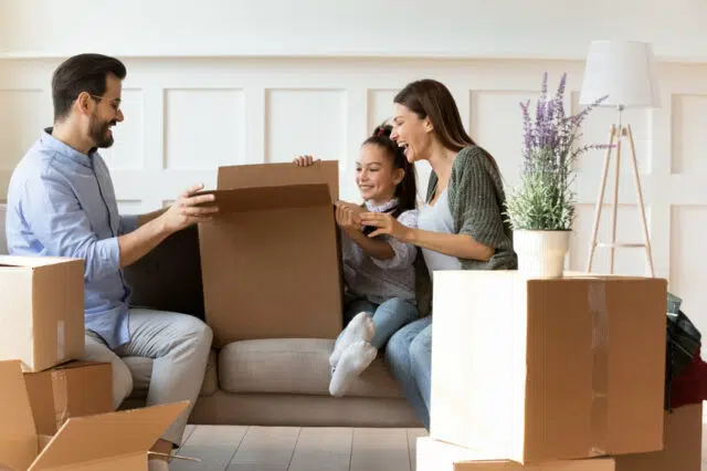 Adorable daughter helping parents with cardboard boxes on moving day
