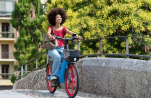 Pourquoi les entreprises françaises misent sur les flottes de vélos électriques partagés pour améliorer le bien-être des employés et réduire leur empreinte carbone Happy black woman riding electric bicycle on city street bridge