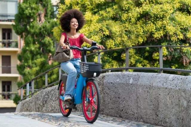 Happy black woman riding electric bicycle on city street bridge Happy black woman riding electric bicycle on city street bridge