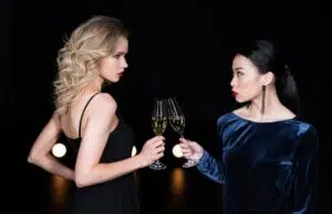 young glamour girls in evening gowns clinking with champagne glasses at party