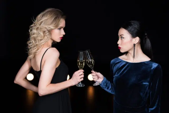 young glamour girls in evening gowns clinking with champagne glasses at party young glamour girls in evening gowns clinking with champagne glasses at party