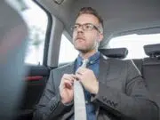 Businessman sitting in back of car, straightening tie