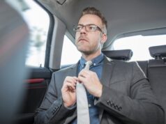 Businessman sitting in back of car, straightening tie