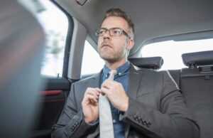 Businessman sitting in back of car, straightening tie