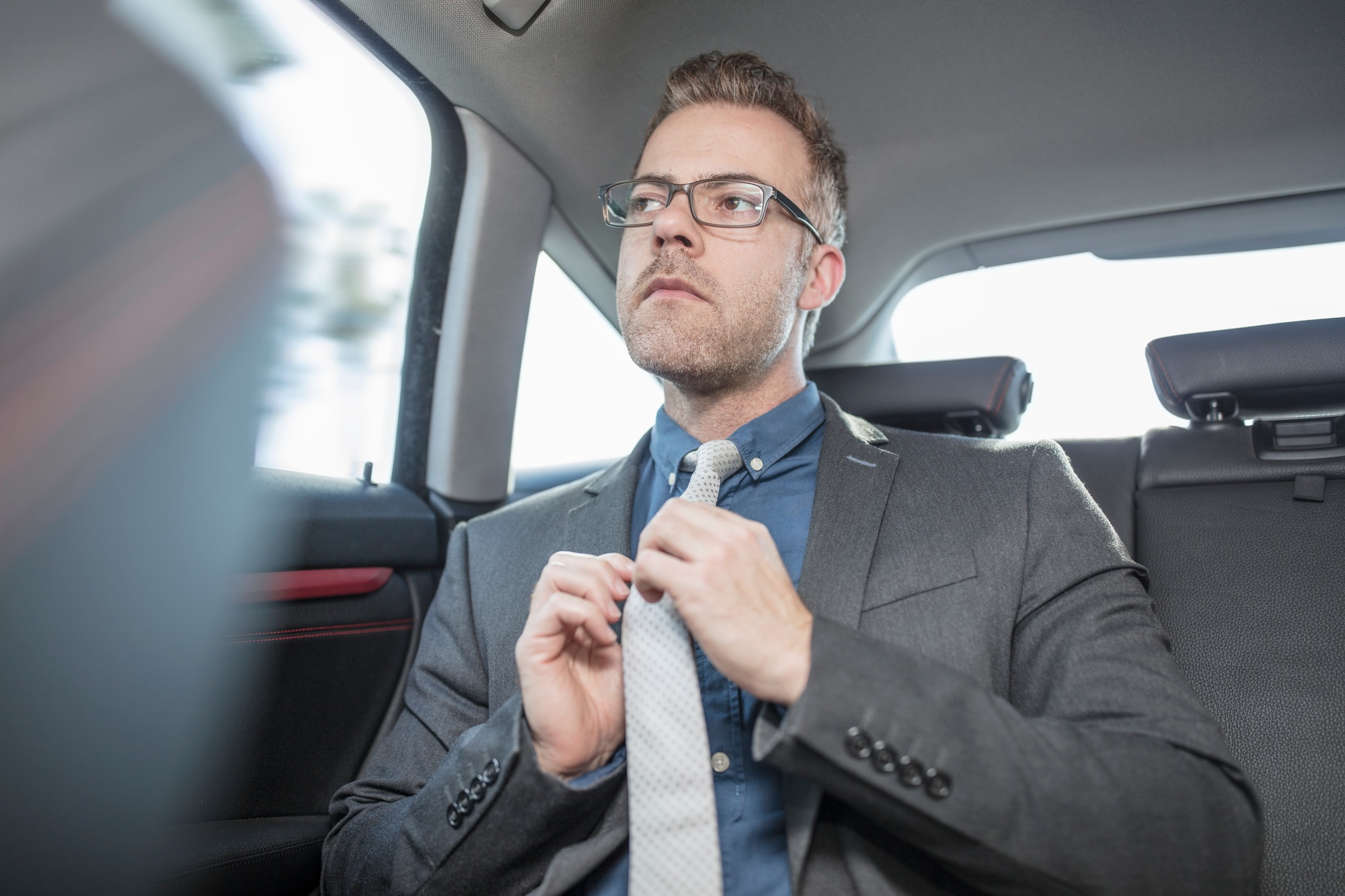 Businessman sitting in back of car, straightening tie