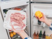 cropped view of woman holding frozen meat and bell pepper near open fridge with fresh food on