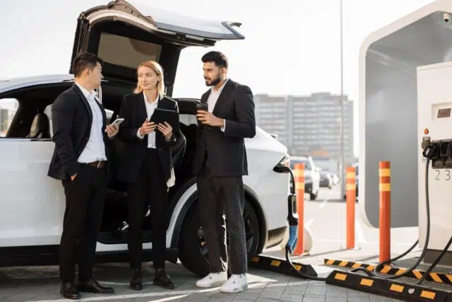 Multiracial businesspeople refilling EV at charging location Multiracial businesspeople refilling EV at charging location