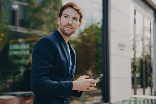 Pensive businessman holds cellular sends text messages dressed formally Pensive businessman holds cellular sends text messages dressed formally