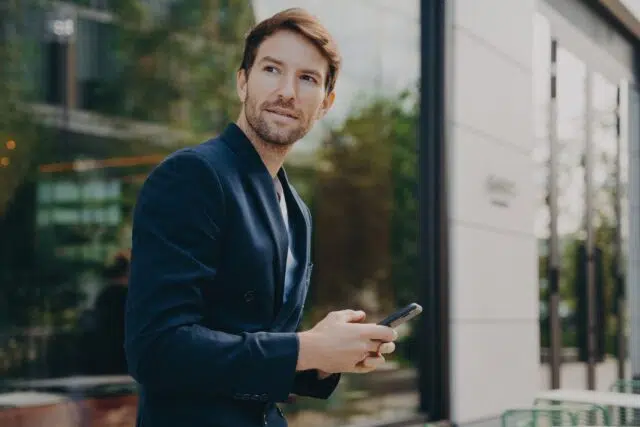 Pensive businessman holds cellular sends text messages dressed formally Pensive businessman holds cellular sends text messages dressed formally