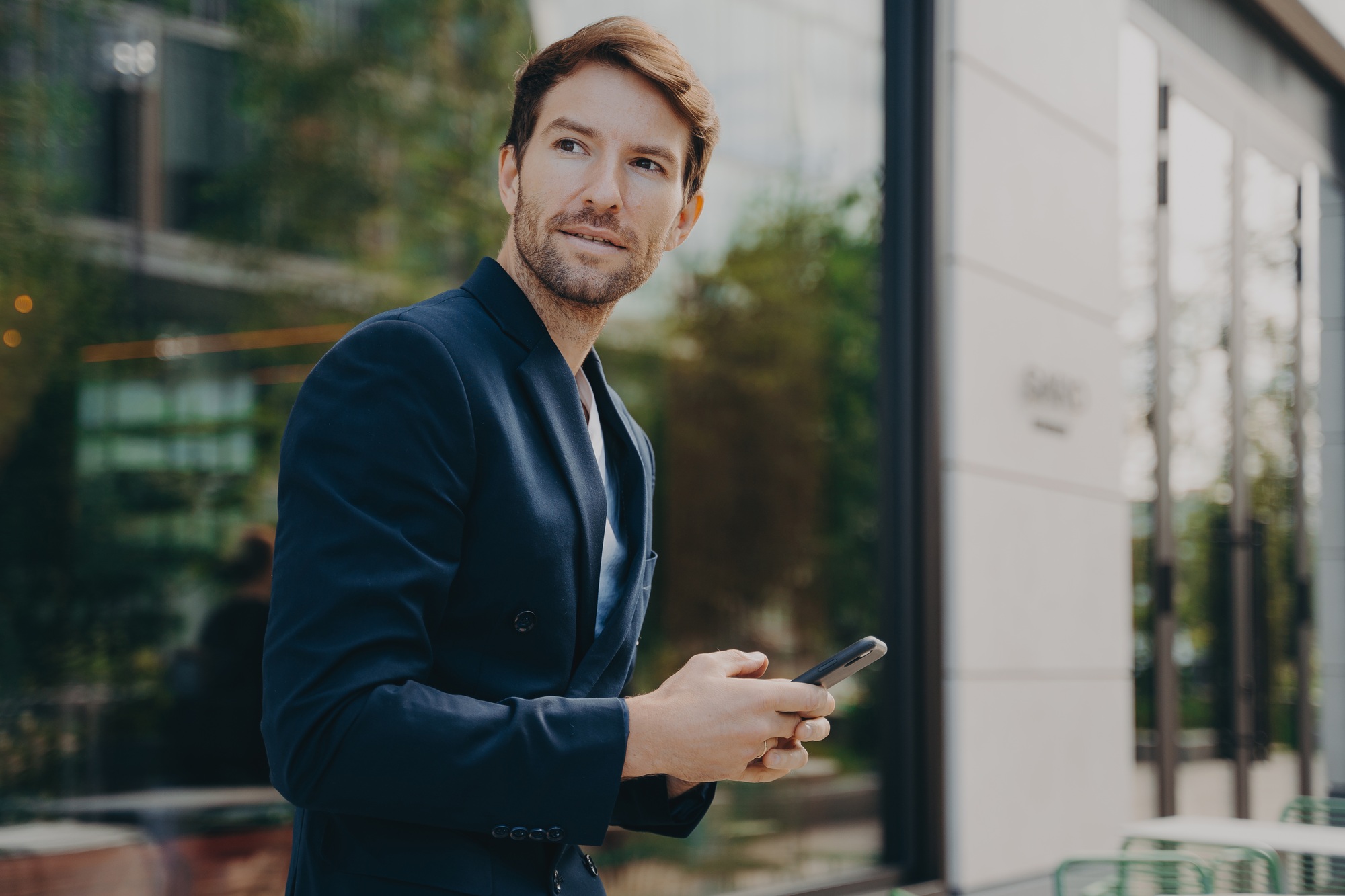 Pensive businessman holds cellular sends text messages dressed formally
