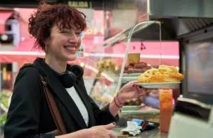 A woman in a black jacket smiles as she receives a plate of food from a man behind a counter.