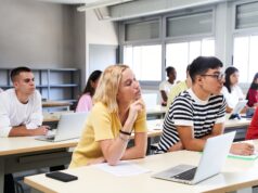 High school science class: A boy and girl using a laptop computer while attending to the teacher