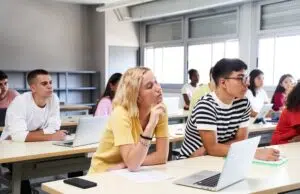 High school science class: A boy and girl using a laptop computer while attending to the teacher