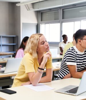High school science class: A boy and girl using a laptop computer while attending to the teacher