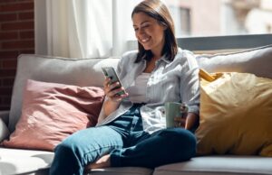 Pretty young smiling woman using mobile phone sitting on a couch at home.