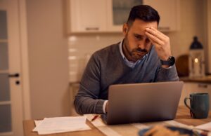 Worried businessman reading problematic e-mail on laptop at home.