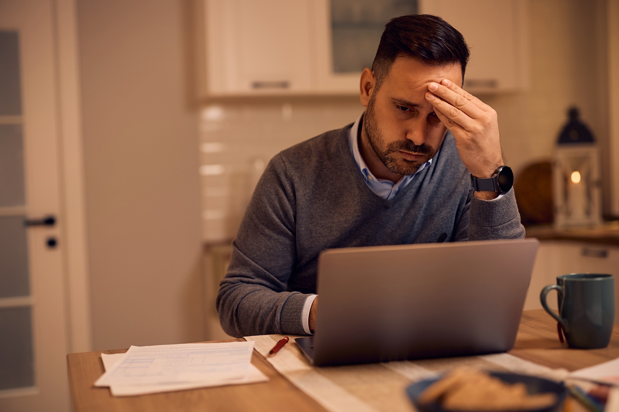 Worried businessman reading problematic e-mail on laptop at home.